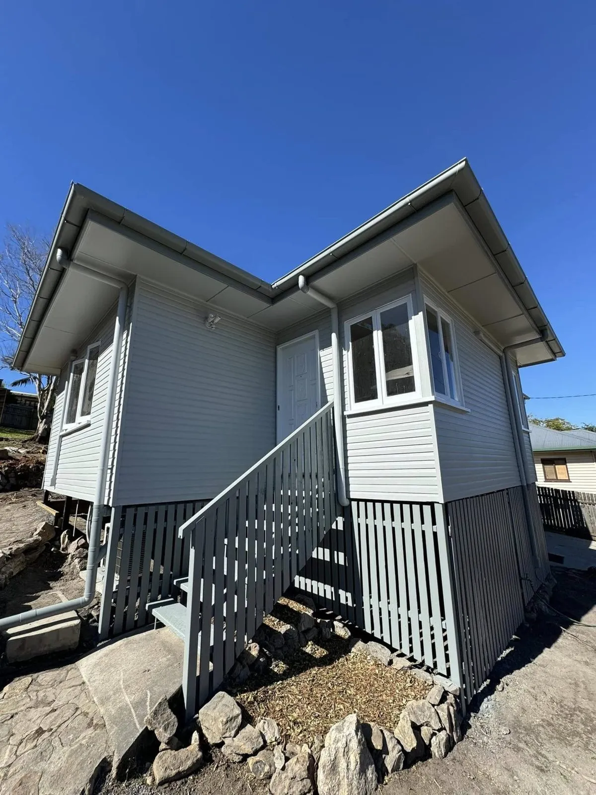 Weatherboard house repainted light grey with white windows and grey stairs