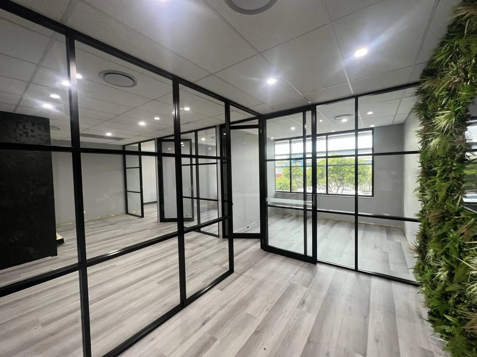 Open office with white walls, black-framed glass partitions and a green plant wall at Rivergate Marina